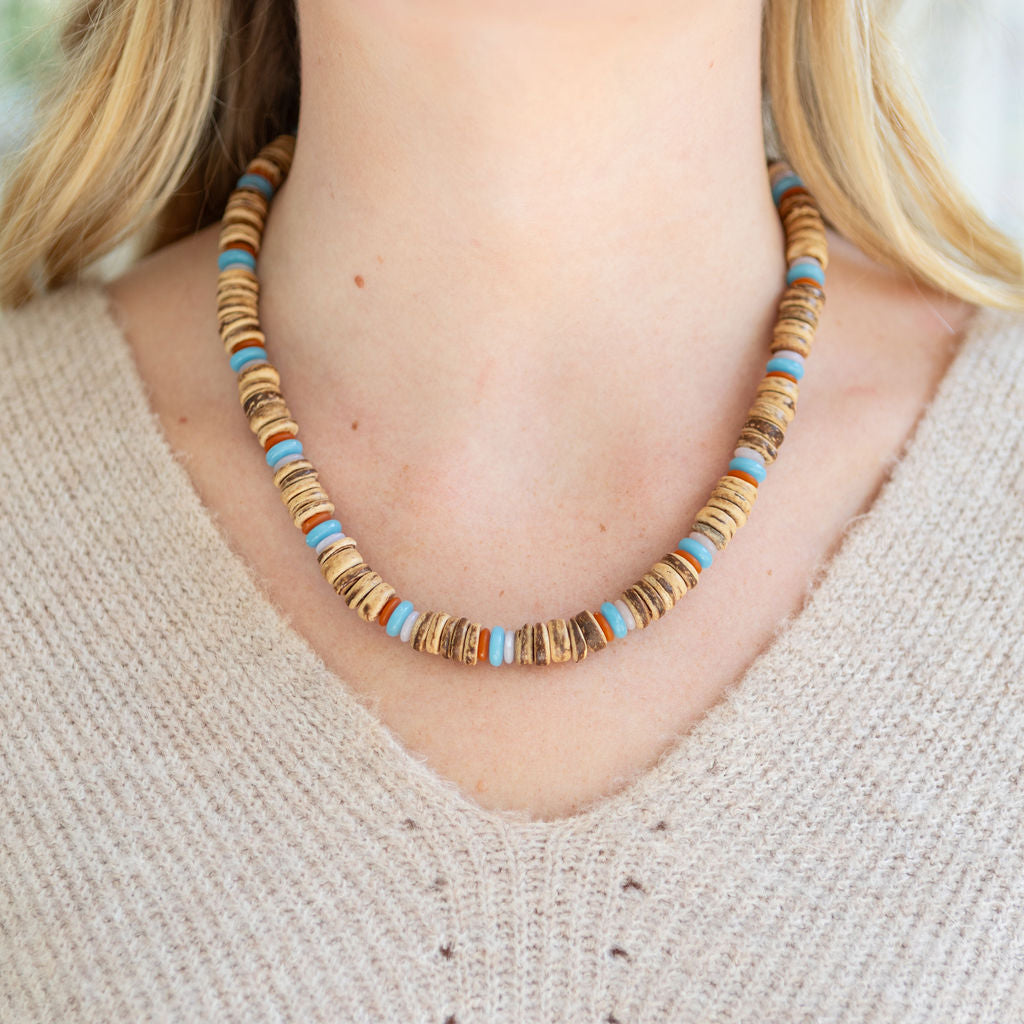 Necklace with brown and blue beads worn by a person in a beige sweater.