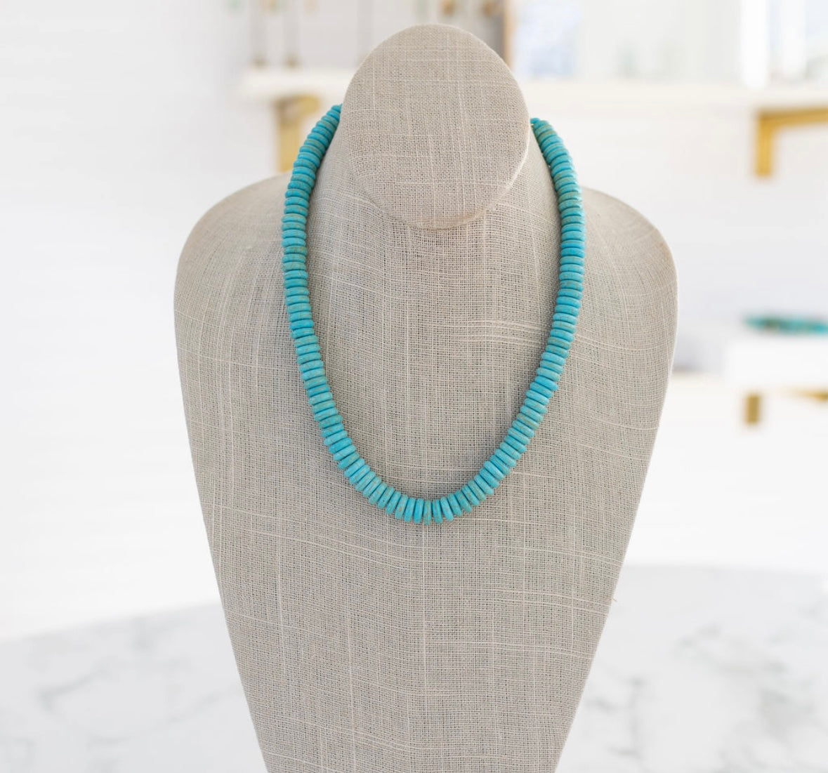 A turquoise gemstone necklace with a gold carabiner clasp on a mannequin neck.