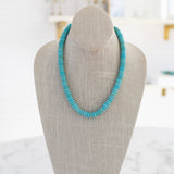 A turquoise gemstone necklace with a gold carabiner clasp on a mannequin neck.