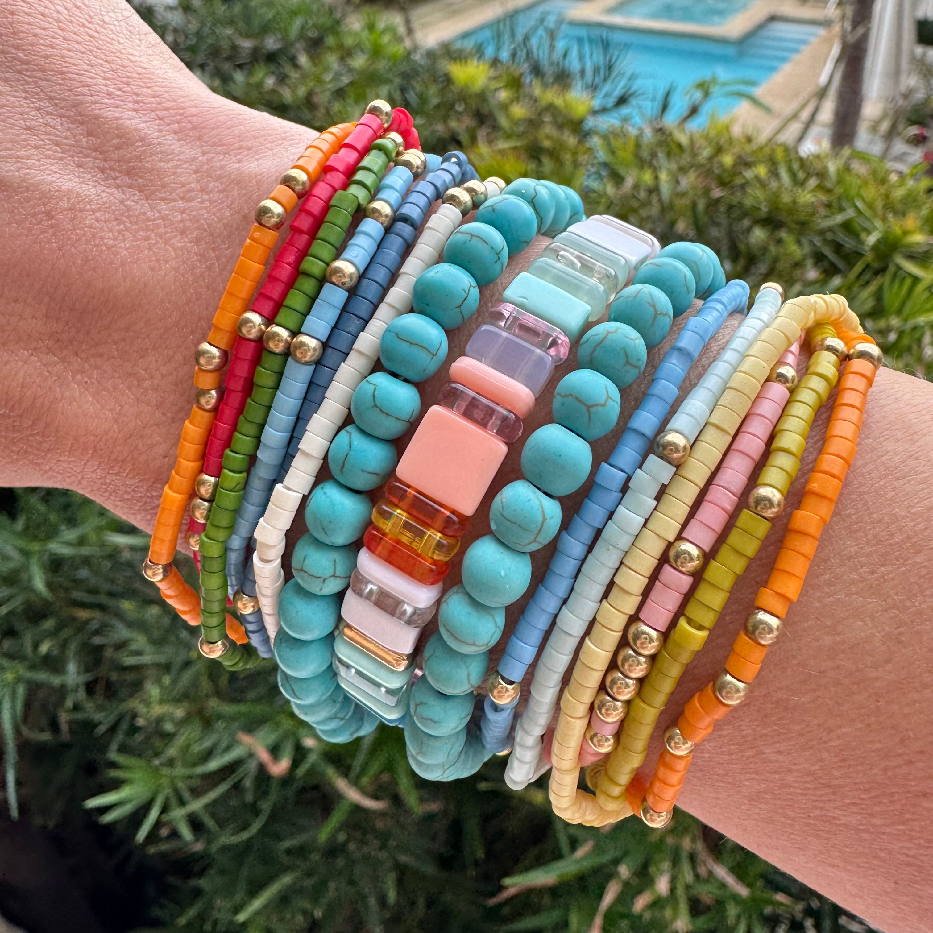 Picture of arm with a bundle of twelve colorful small beaded bracelets, two large bead turquoise bracelets and one square beaded bracelet