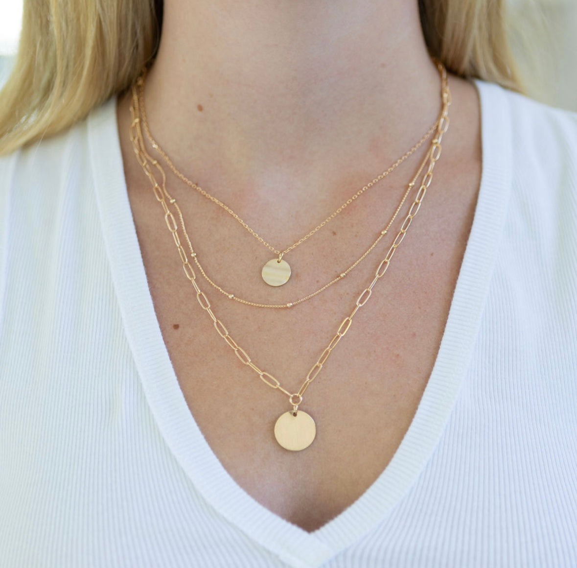 Gold necklace stack with disc pendants on a person wearing a white top