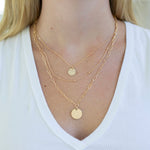Gold necklace stack with disc pendants on a person wearing a white top