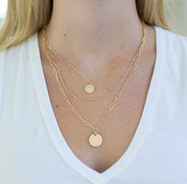 Gold necklace stack with disc pendants on a person wearing a white top