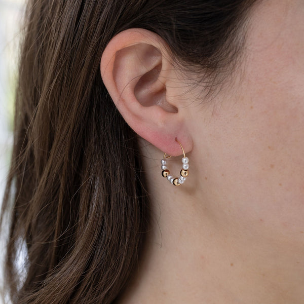 Picture of model wearing a find gold hoops threaded with pearl and gold beads.