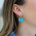 Picture of woman wearing a pair of dangle earrings. Earrings are small gold hoops with a larger turquoise disc bead dangling from it.
