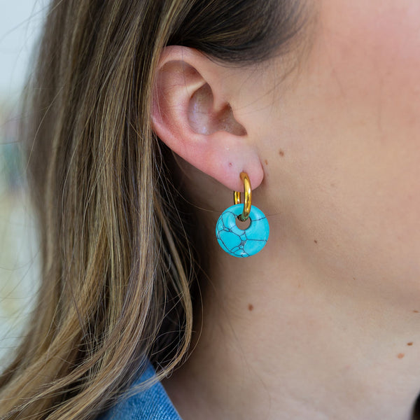 Picture of woman wearing a pair of dangle earrings. Earrings are small gold hoops with a larger turquoise disc bead dangling from it.