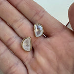 Picture of a hand holding clear stone halfmoon Studs in a gold setting.