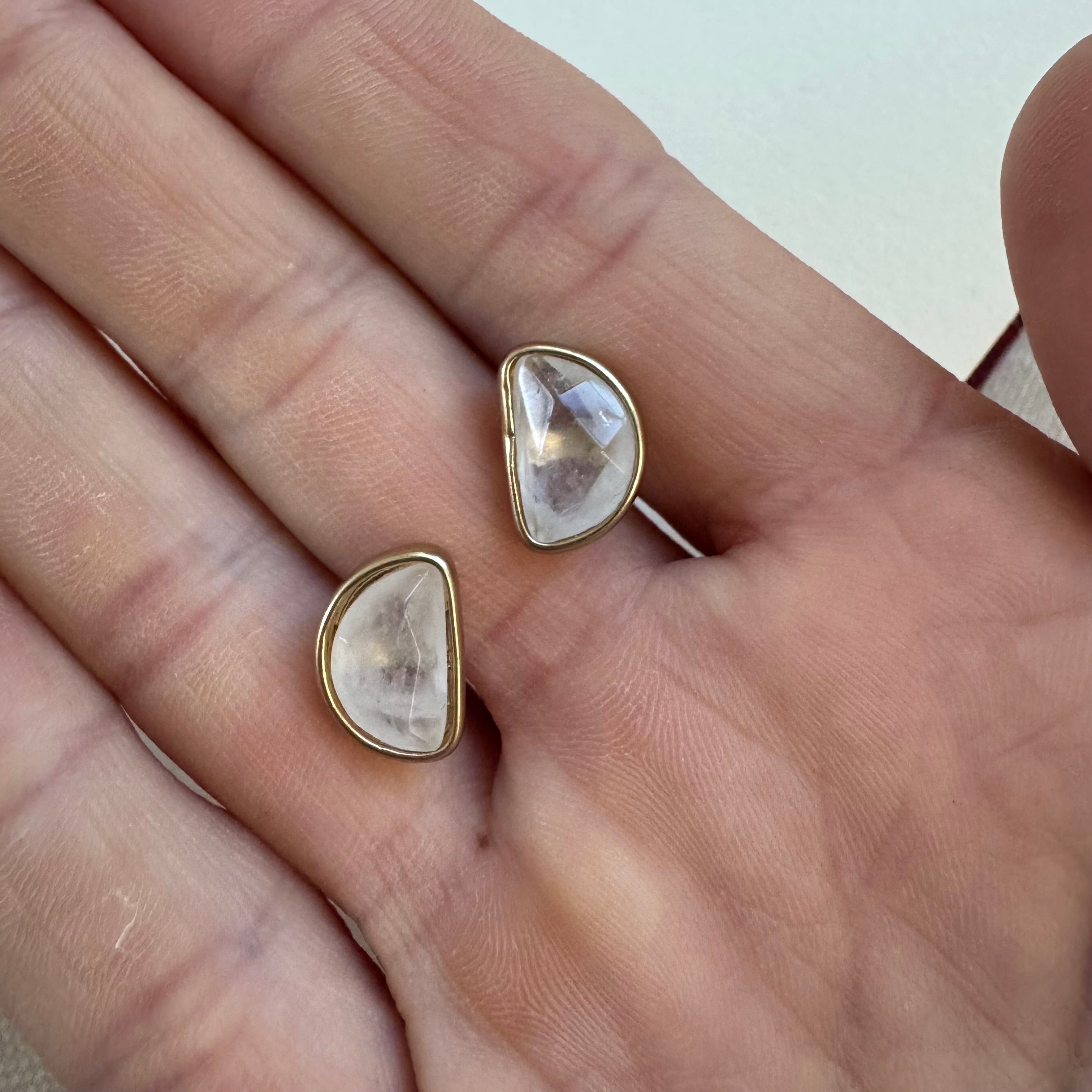 Picture of a hand holding clear stone halfmoon Studs in a gold setting.