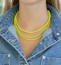 Neon yellow triple strand chain necklace worn by a person in a denim jacket.