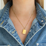 Gold necklace with an envelope pendant worn by a person in a denim jacket.