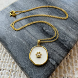 Gold necklace with a paw print pendant on a gray stone surface