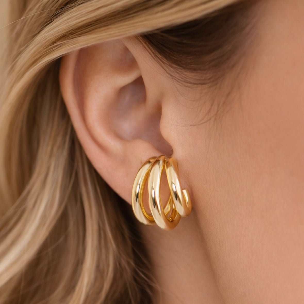 Close-up of a three hoop gold hoop earring worn by a person with blonde hair.
