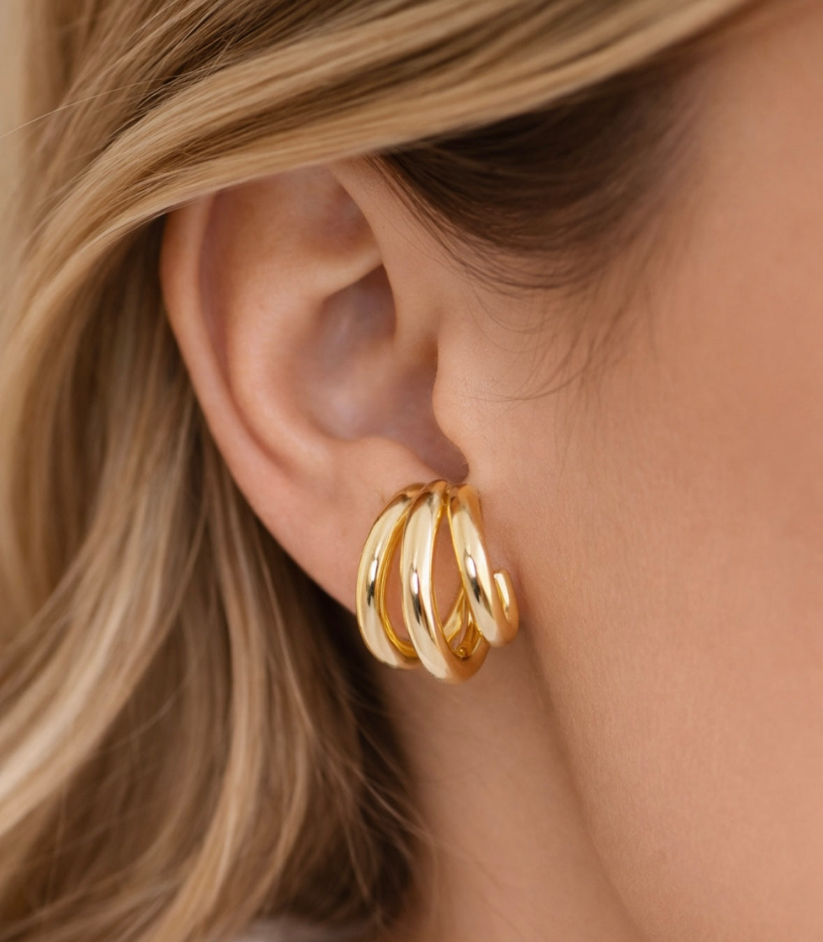 Close-up of a three hoop gold hoop earring worn by a person with blonde hair.