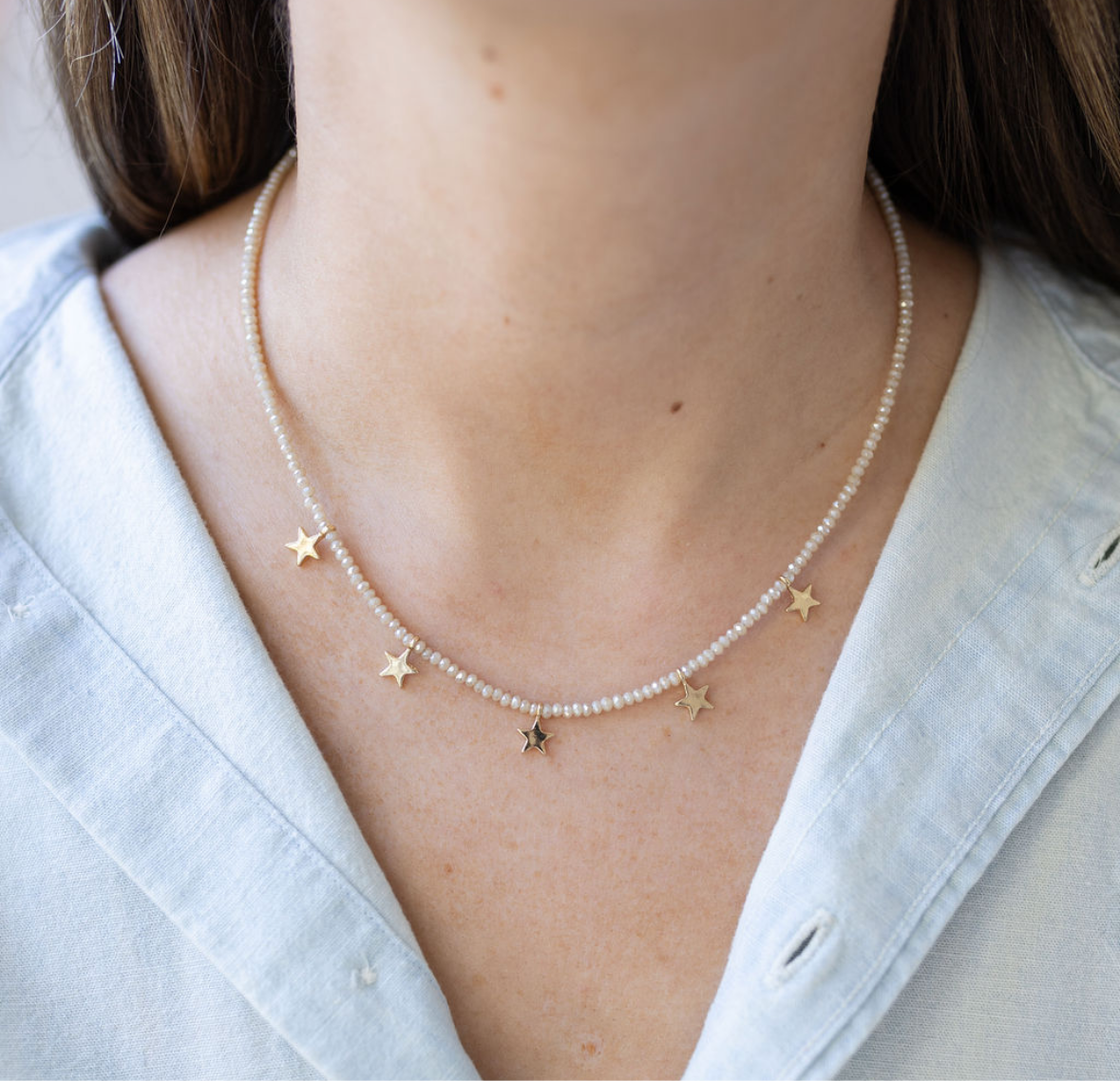 Picture of a dainty white seed bead necklace with tiny gold star beads dangling from it.