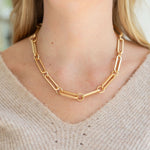 Gold chain necklace worn by a person with a neutral background