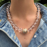 Clear beaded necklace with a gold accent worn by a person in a denim jacket.