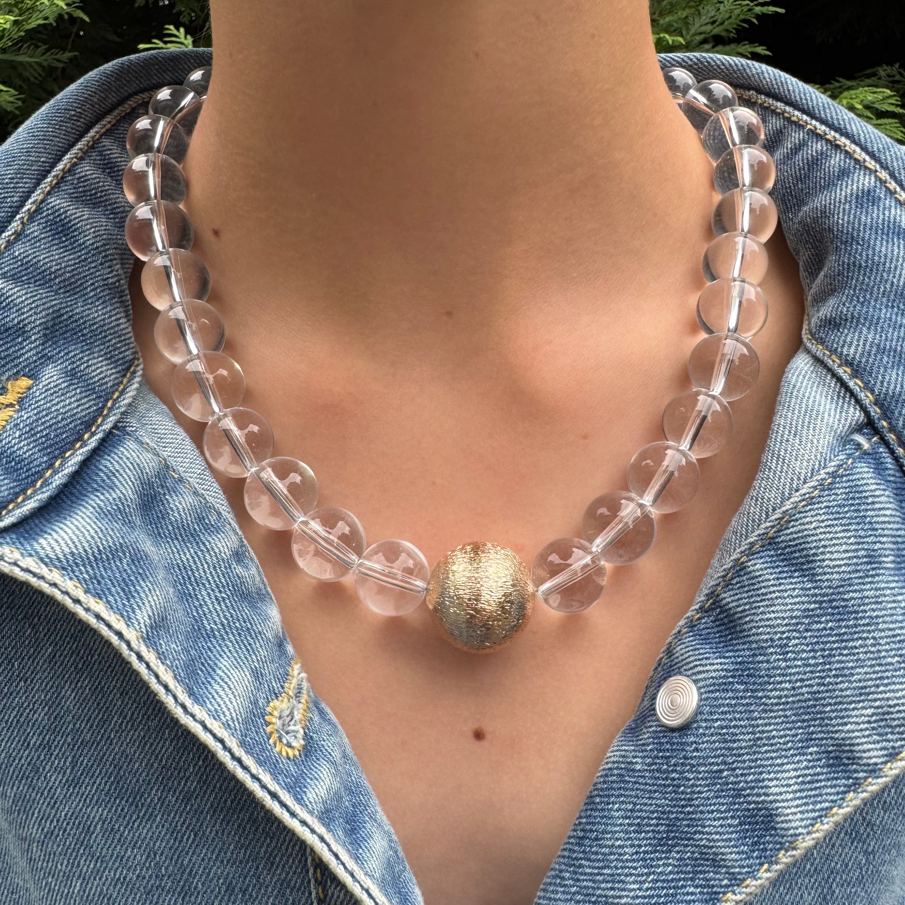 Clear beaded necklace with a gold accent worn by a person in a denim jacket.