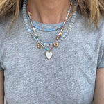 A person wearing three layered necklaces with varying designs and beads, predominantly in blues and gold colors.