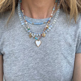 A person wearing three layered necklaces with varying designs and beads, predominantly in blues and gold colors.
