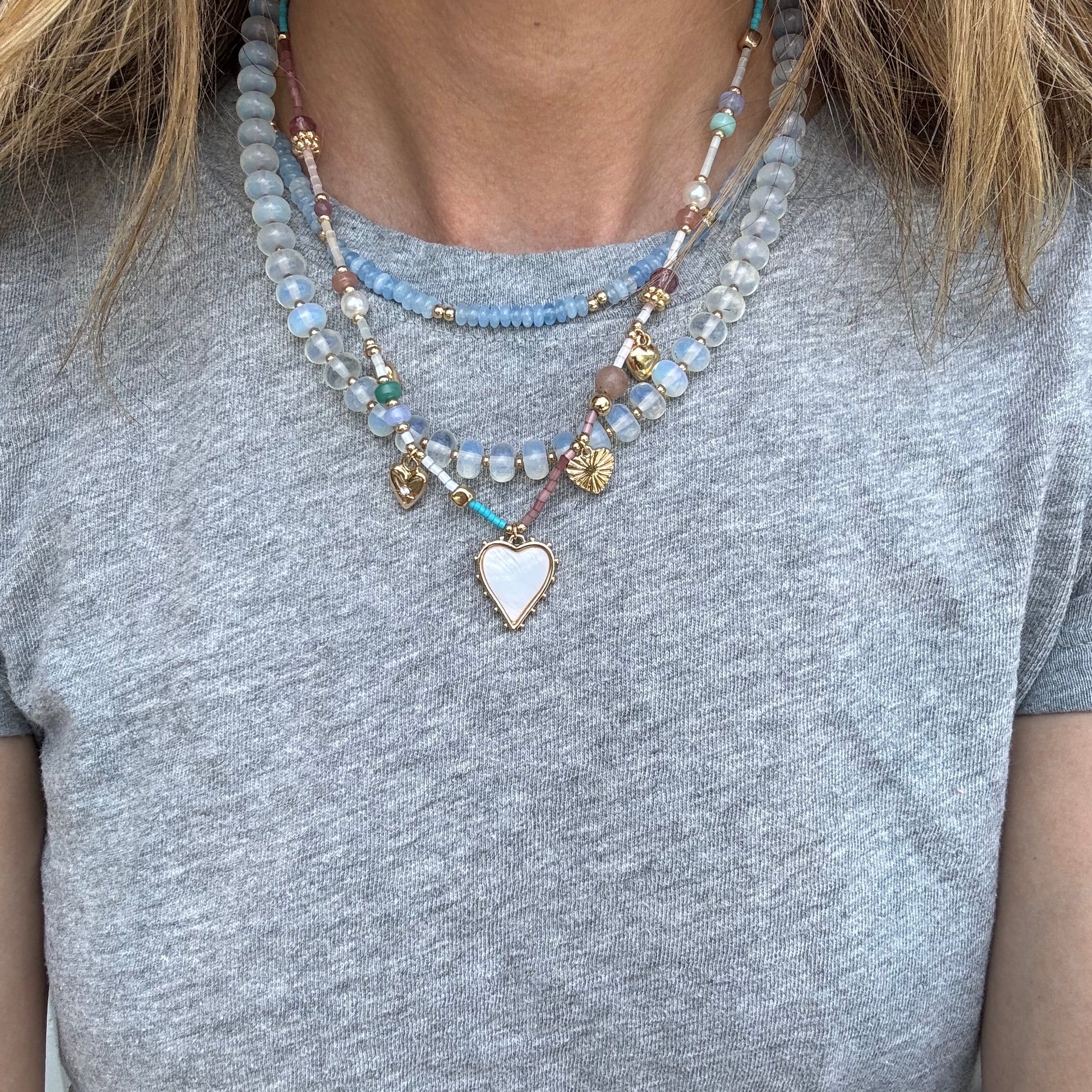 A person wearing three layered necklaces with varying designs and beads, predominantly in blues and gold colors.