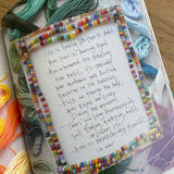 Handwritten text on a piece of paper with colorful bead border, placed on a fabric surface with yarn.