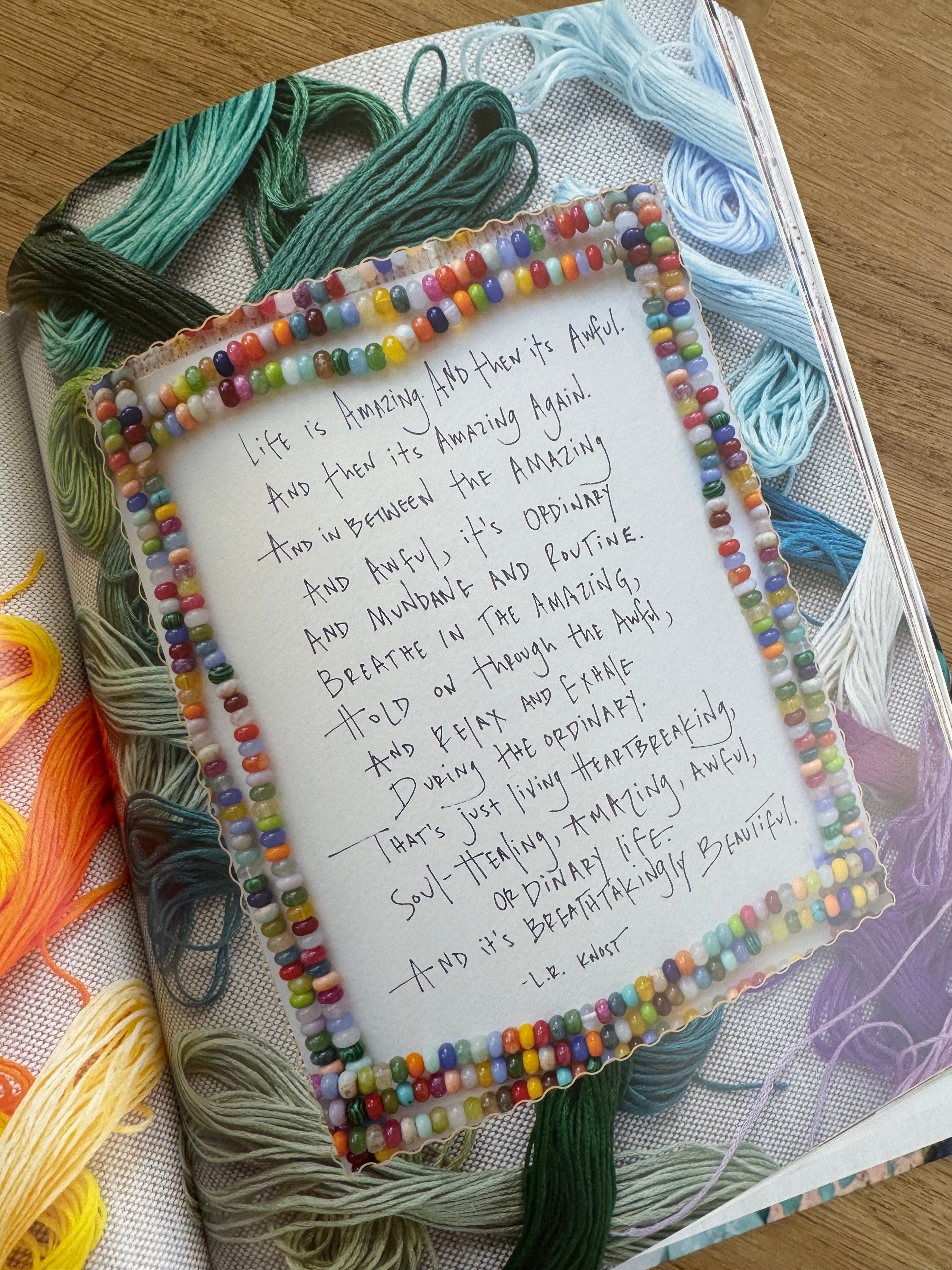 Handwritten text on a piece of paper with colorful bead border, placed on a fabric surface with yarn.