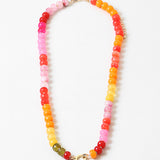Large bead necklace made of orange, pinks and yellows with a large gold clasp at its center.
