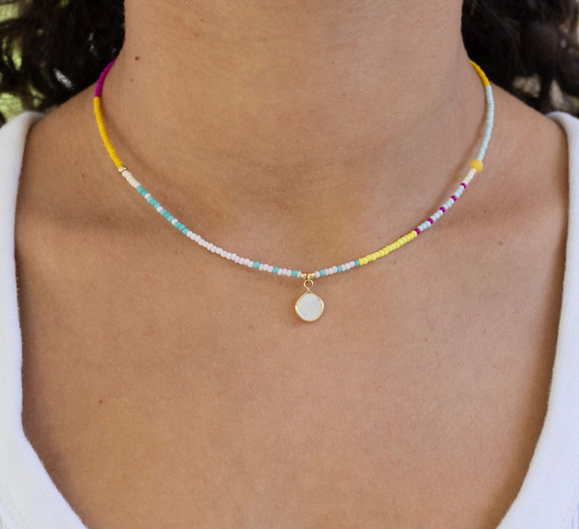 Dainty bead necklace in white, teal, yellow and pink with a small white enamel disc pendant.