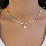 Dainty bead necklace in white, teal, yellow and pink with a small white enamel disc pendant.