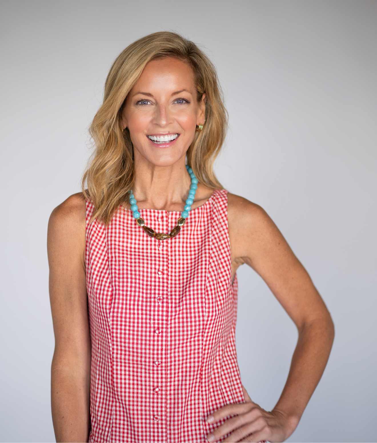 Woman wearing a red checkered dress with a blue necklace against a gray background
