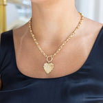 Woman wearing a gold chain toggle necklace with a gold heart medallion that says Love on it