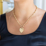 Woman wearing a gold chain toggle necklace with a gold heart medallion that says Love on it