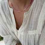 Picture of a woman in a white blouse wearing a dainty white and pink bead necklace.