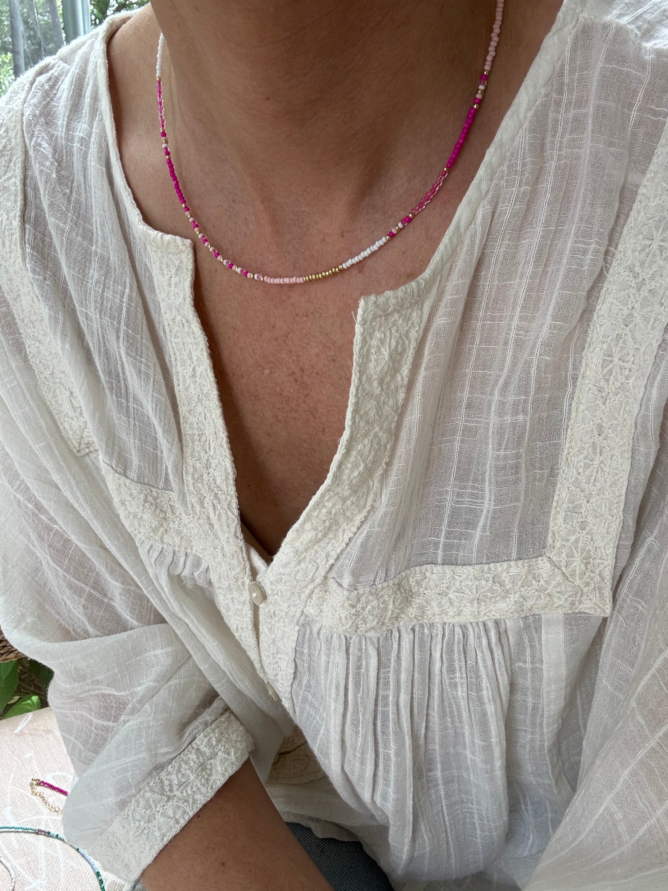 Picture of a woman in a white blouse wearing a dainty white and pink bead necklace.