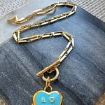 Gold chain necklace with a blue heart locket pendant on a textured surface