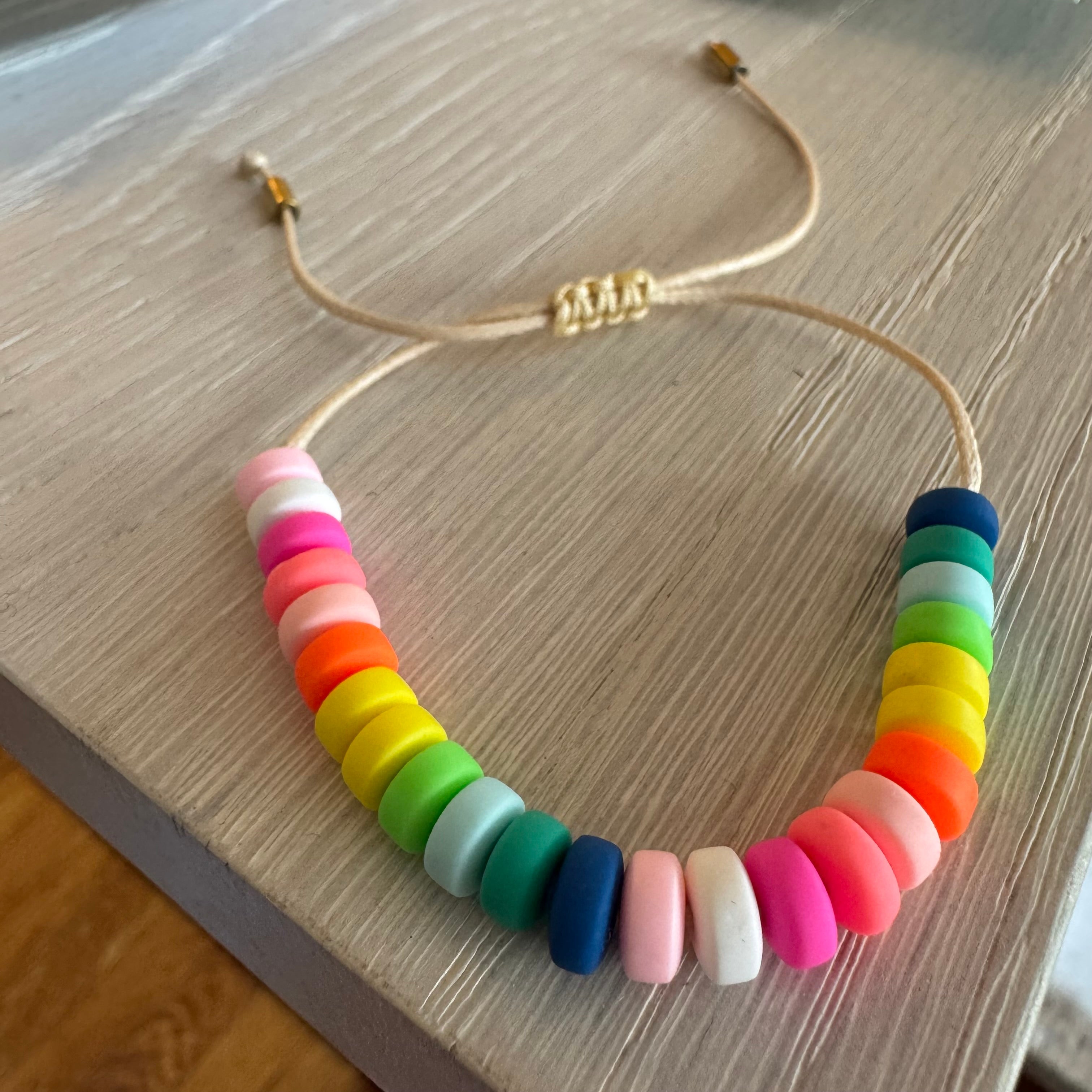Picture of a cord bracelet with brightly colored resin beads in blue, greens, yellow, orange, pinks and white.