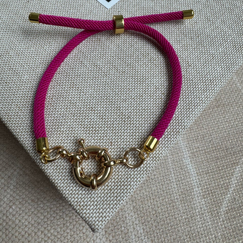 Picture of a dark pink woven slider bracelet with gold accents and a gold toggle clasp at it's center.