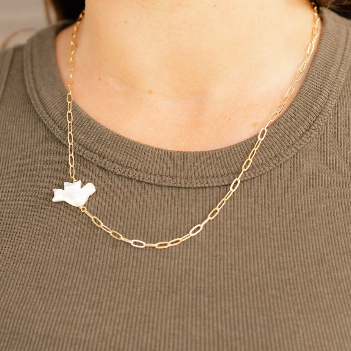 Gold chain necklace with a white pendant worn by a person on a plain background