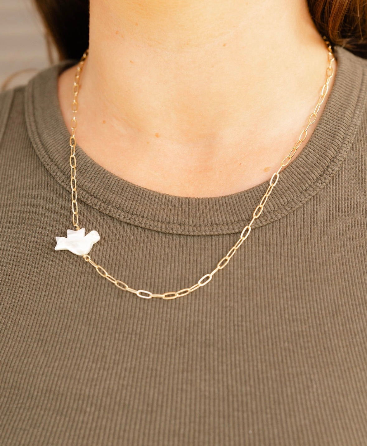 Gold chain necklace with a white pendant worn by a person on a plain background