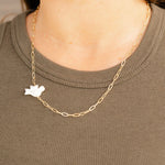 Gold chain necklace with a white pendant worn by a person on a plain background