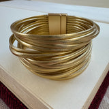 Gold cuff bracelet made of many gold faux leather strands.