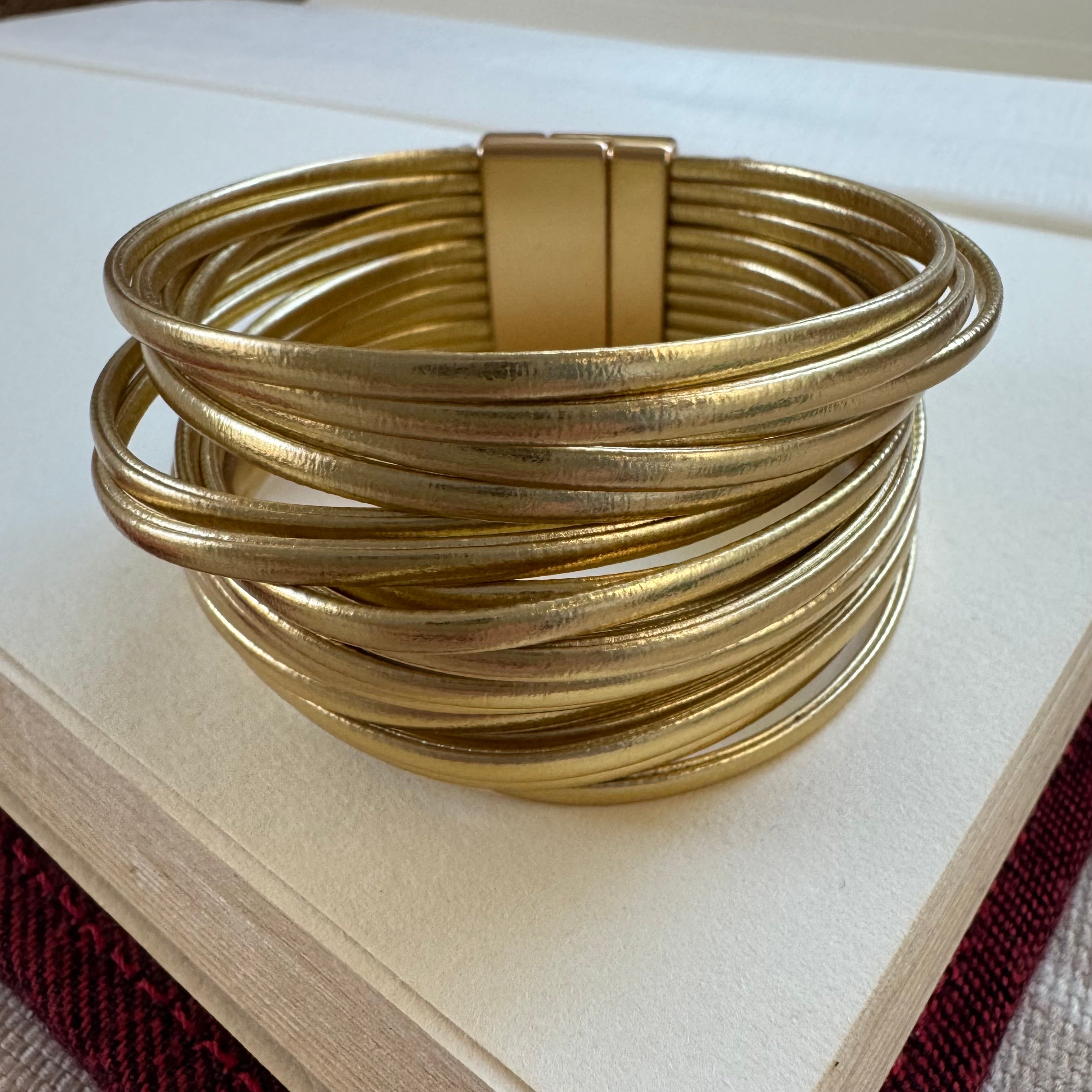 Gold cuff bracelet made of many gold faux leather strands.