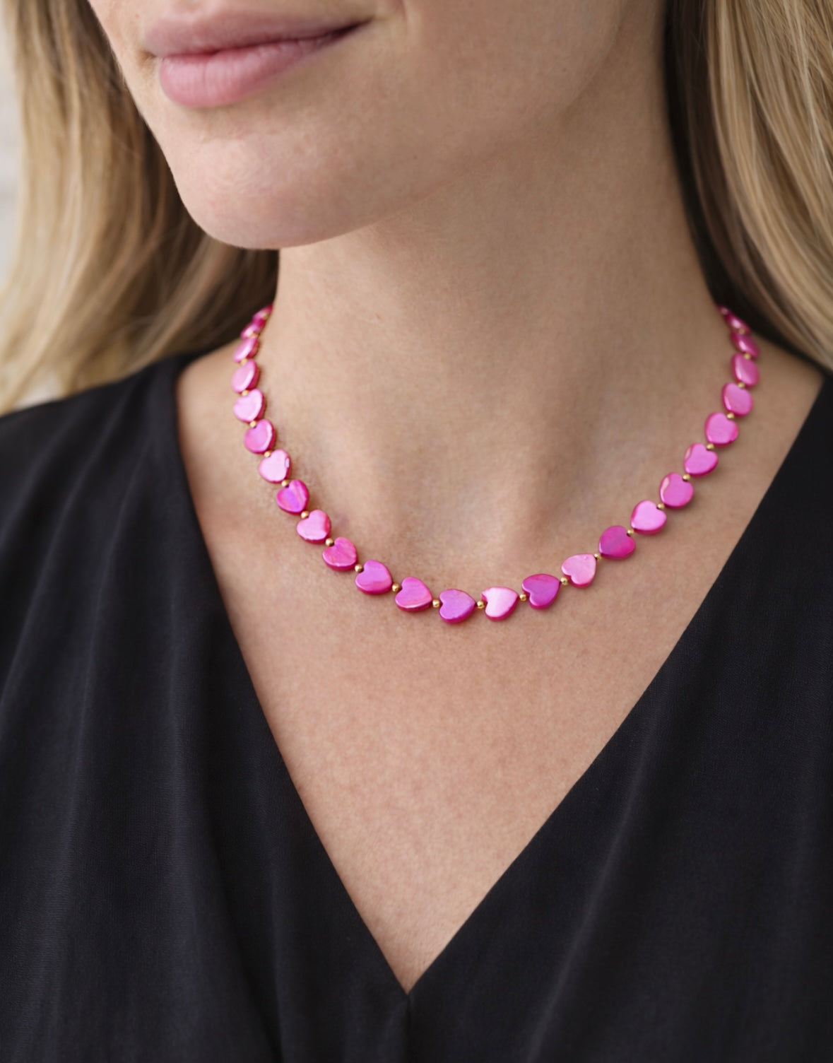 Close-up of a woman wearing a pink heart-shaped beaded necklace against a neutral background