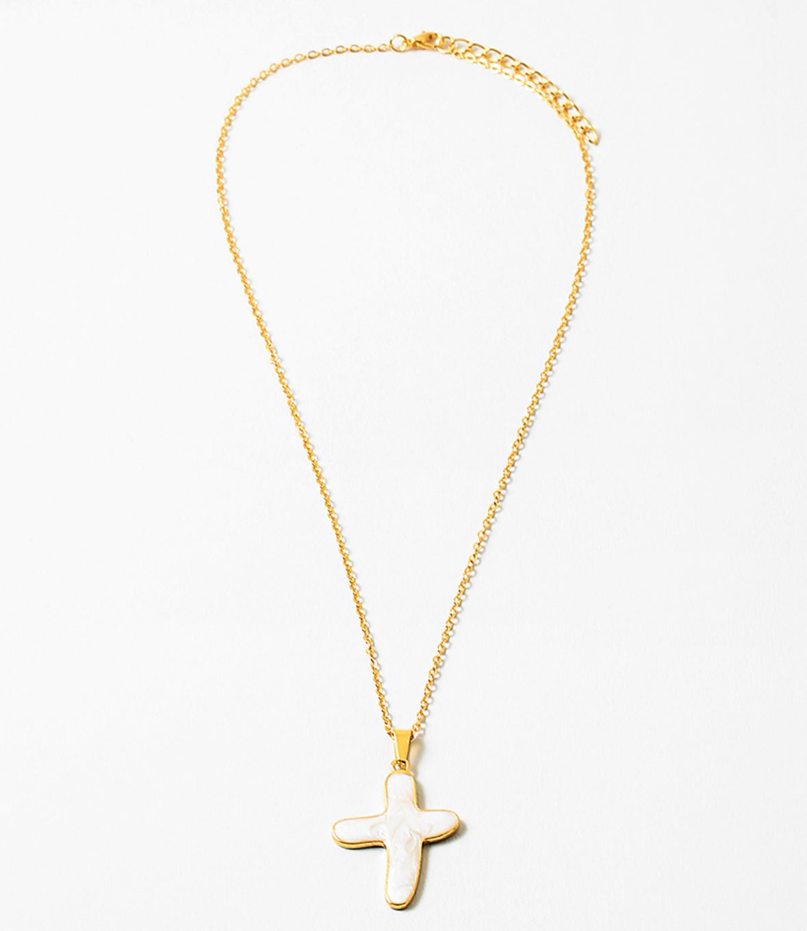 Delicate gold chain necklace with a white cross pendant.