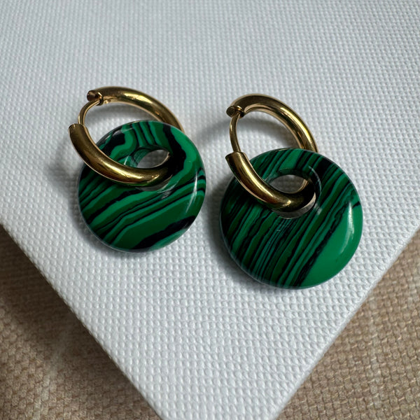 Gold hoop earrings threaded through a large resin green striped bead.