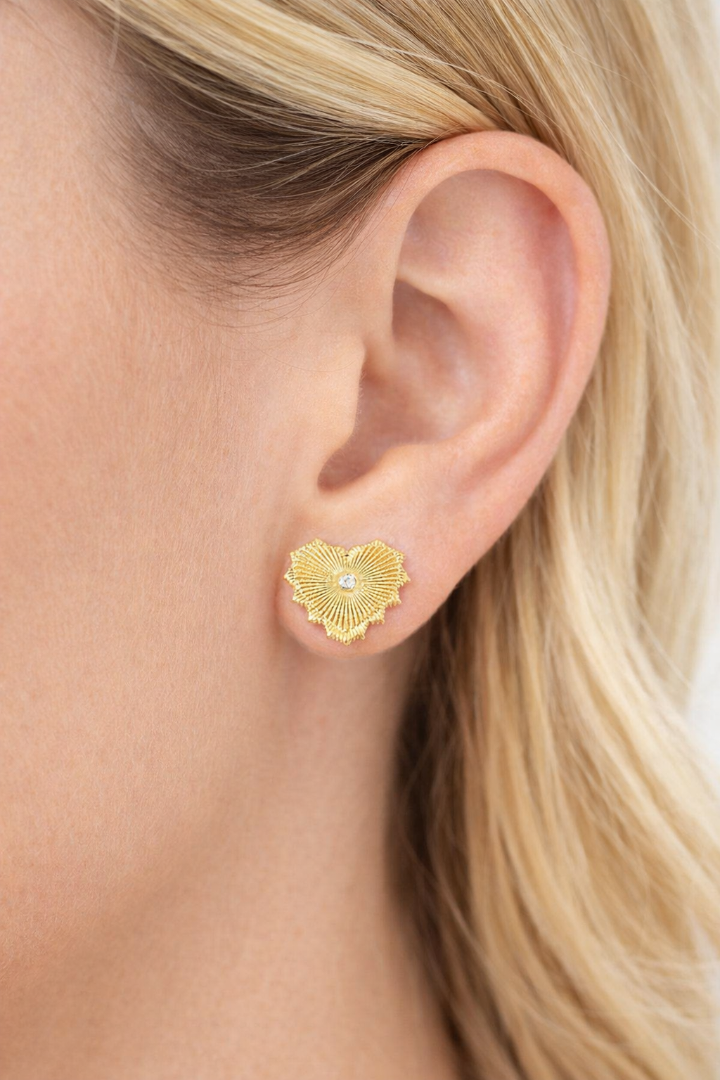 Gold textured heart earring worn by a person with blonde hair.
