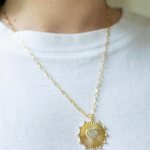 Girl wearing a necklace around her neck with a gold thin chain with a sun/heart medallion attached to it