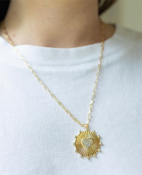 Girl wearing a necklace around her neck with a gold thin chain with a sun/heart medallion attached to it