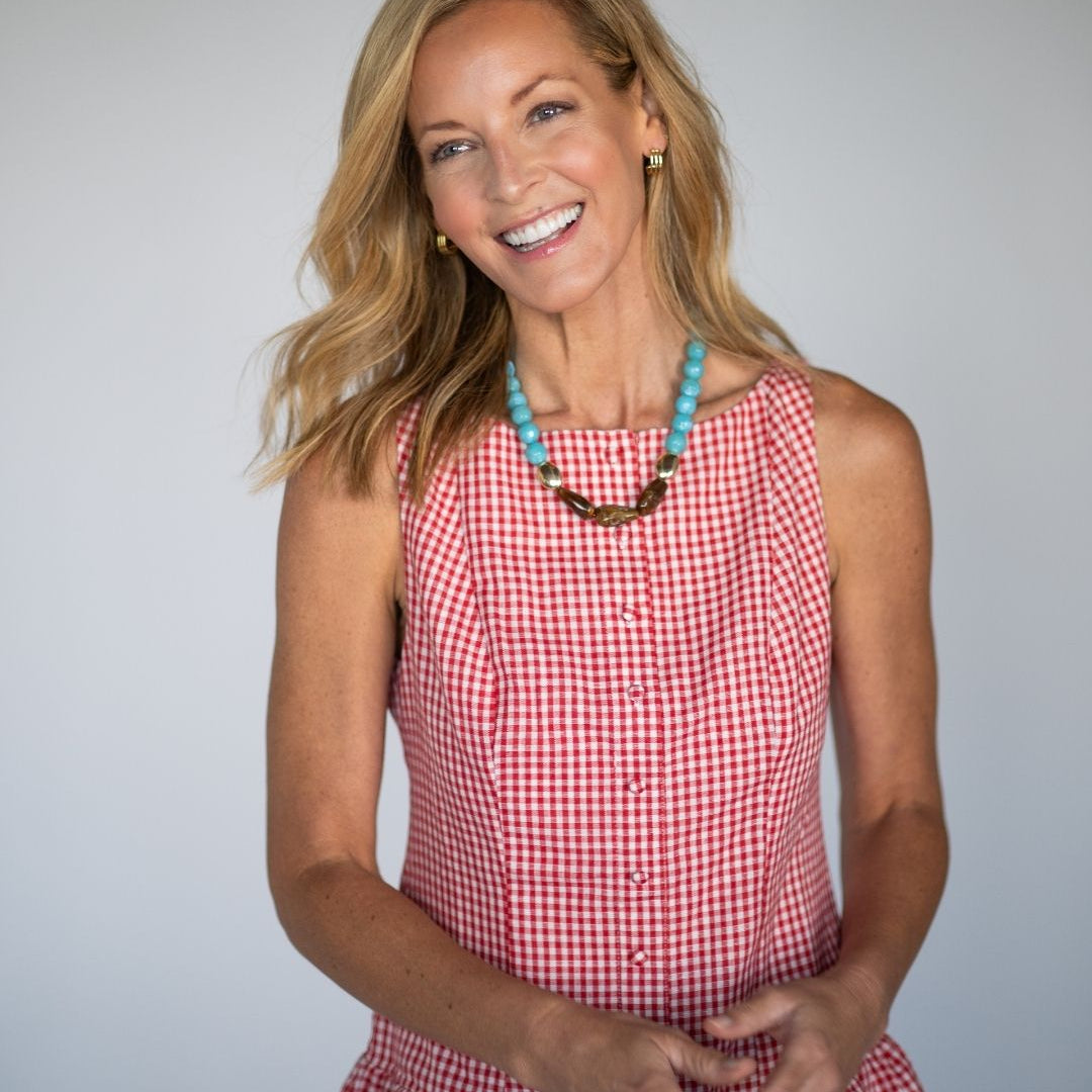 Woman wearing a red checkered dress with a blue and brown statement necklace against a gray background