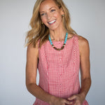 Woman wearing a red checkered dress with a blue and brown statement necklace against a gray background
